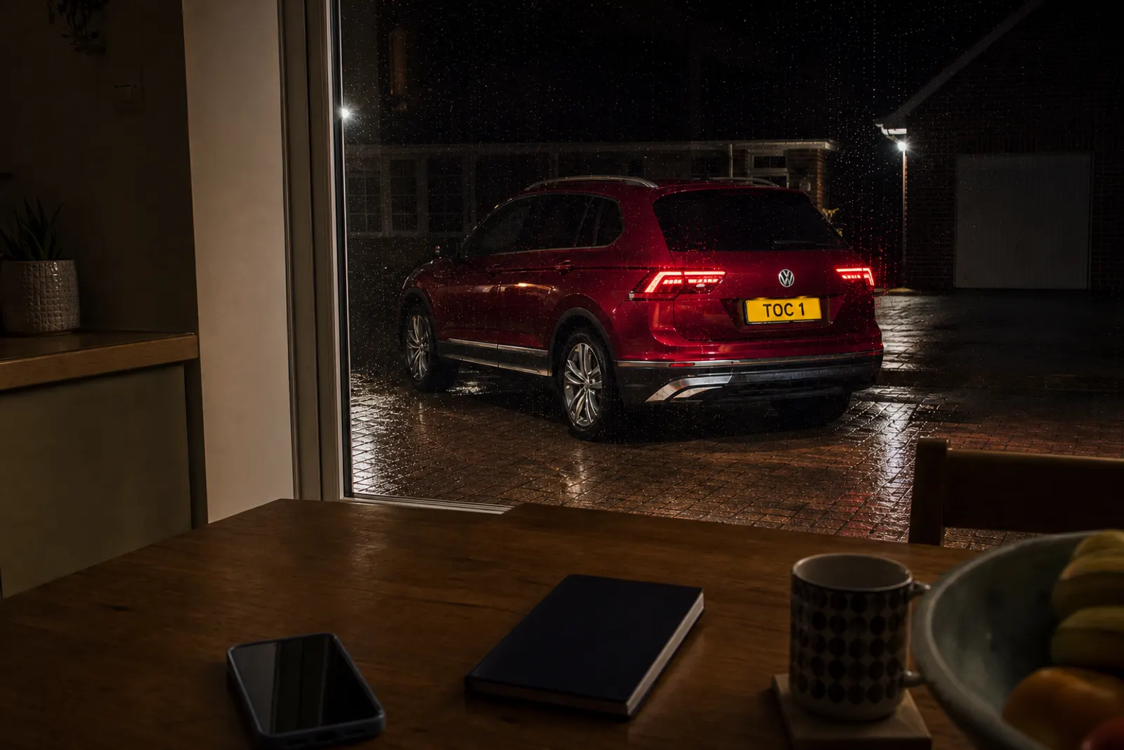 Closed logbook and phone on a table, with a ruby red Volkswagen Tiguan (plate TOC 1) outside