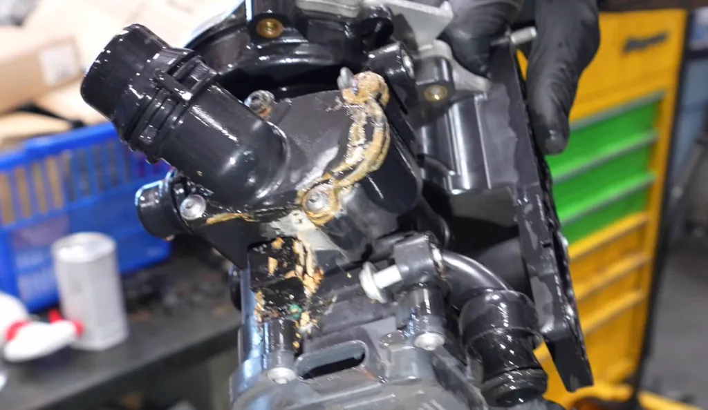 Failed EA888 Gen 3 plastic water pump / thermostat housing with dried coolant crust — workshop demonstration frame from YouTube (not an Owners Club owner photo)